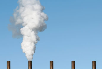 Line of chimney tops against blue sky with smoke emerging from one